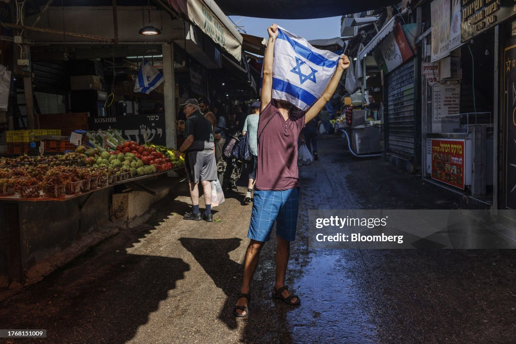 Un client brandit un drapeau national israélien au marché Carmel de Tel Aviv, en Israël, le mardi 7 novembre 2023.. Source : Bloomberg
